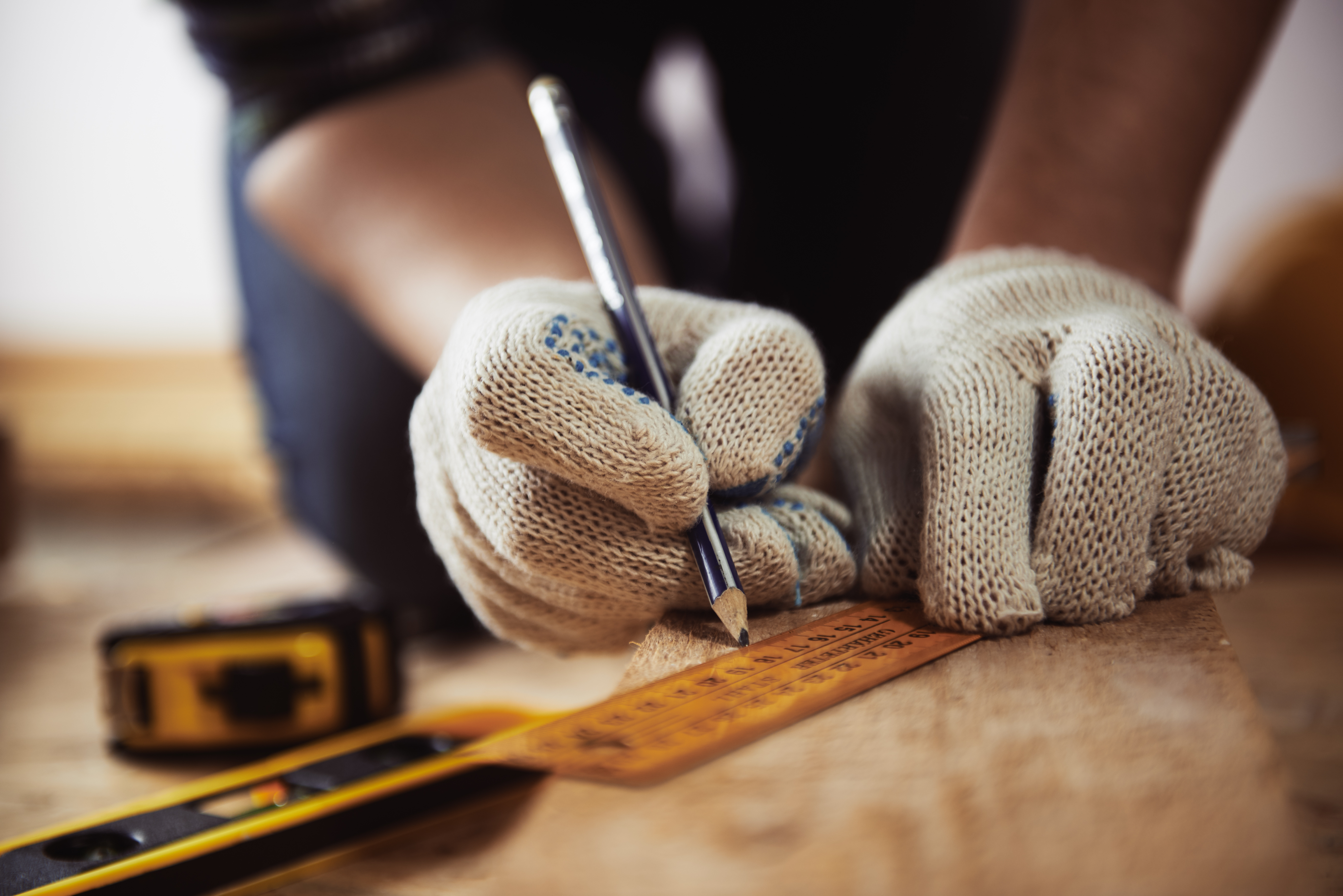 Close-up of craftsman hands in protective gloves measuring woode
